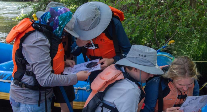 A group of people wearing sun hats and life jackets examine maps.